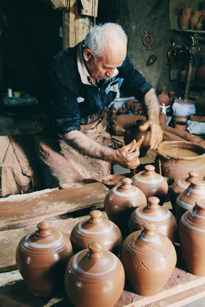 An elderly potter skillfully crafting clay vases in a rustic workshop setting.