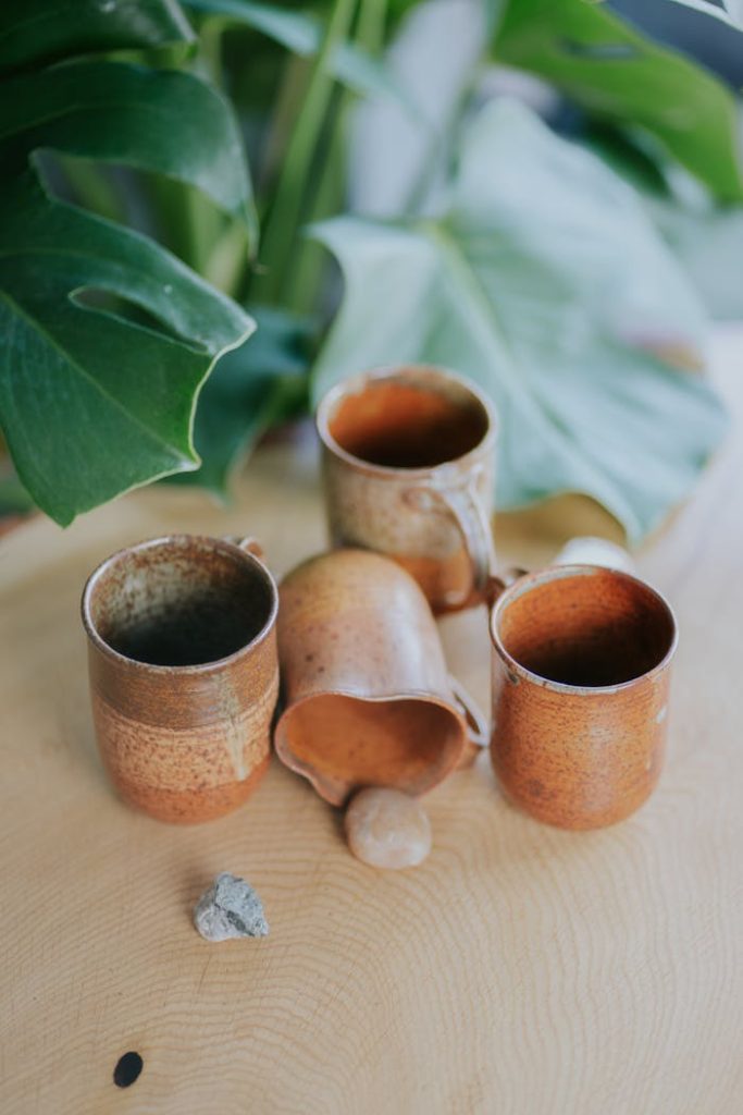 Handcrafted clay mugs and cups set against lush monstera leaves, showcasing natural artistry.