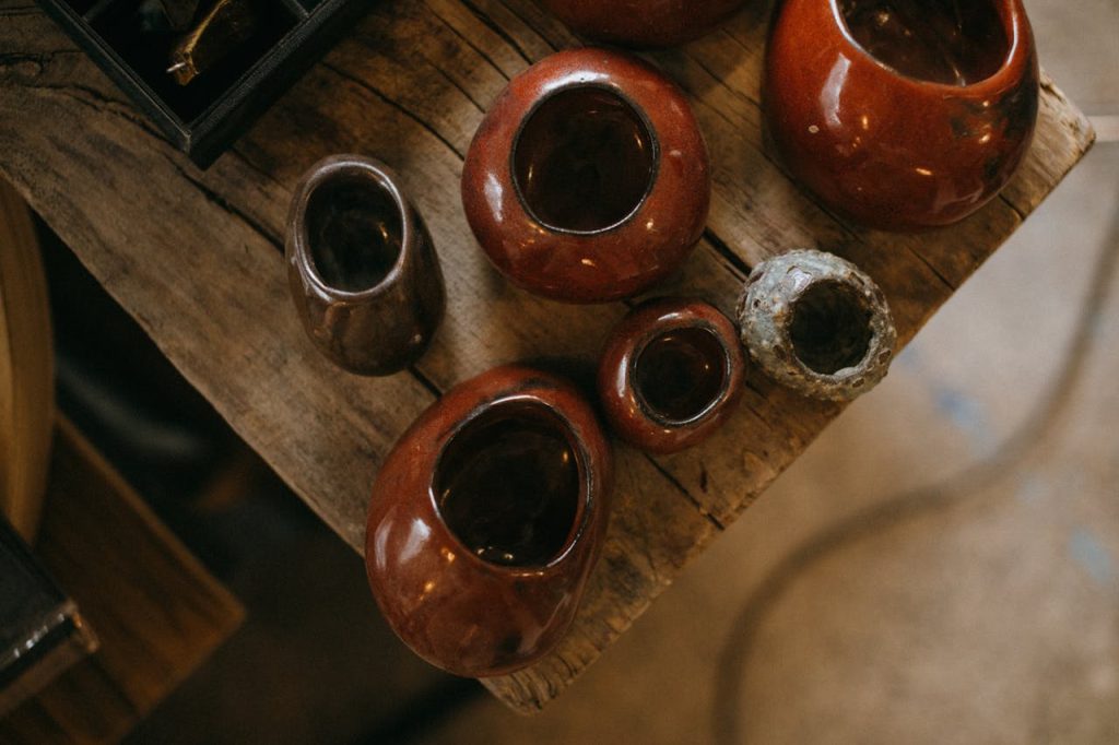 A collection of handmade ceramic pots with rich brown glaze on a rustic wooden table.